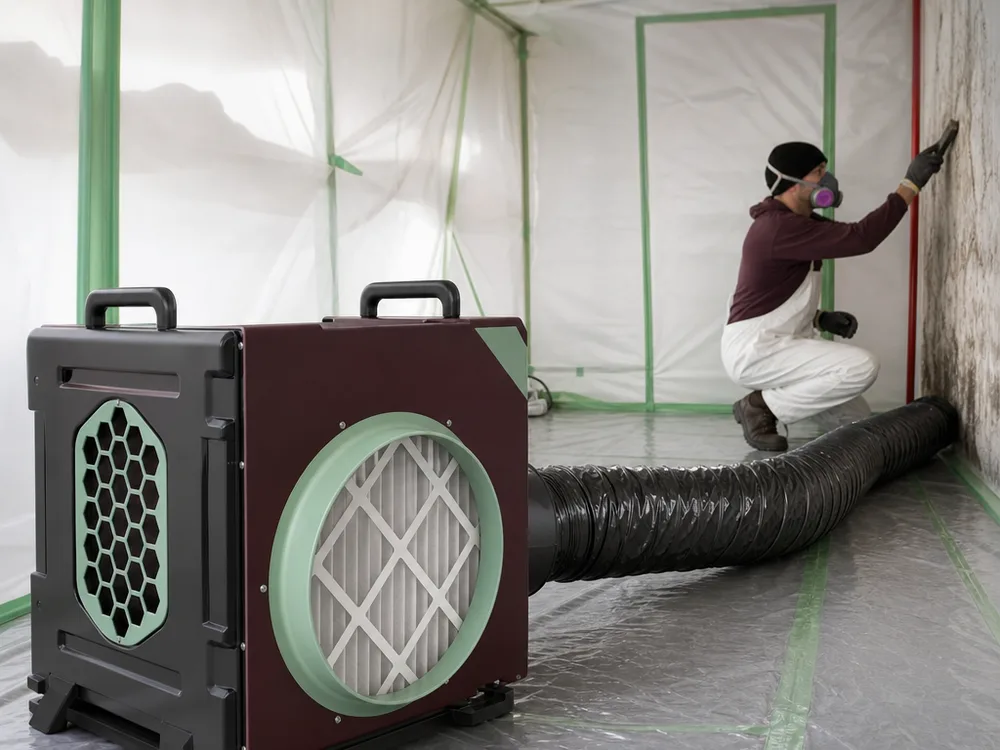 HEPA air scrubber running inside a contained room with flexible ducting angled toward the work zone