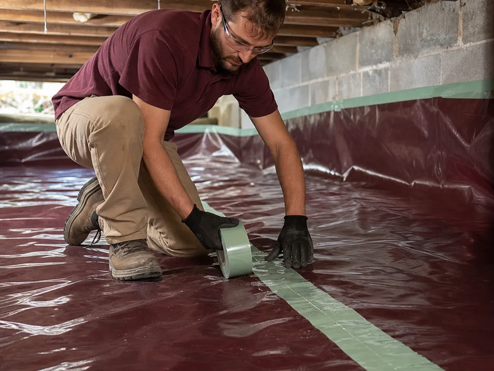 Contractor installing reinforced polyethylene vapor barrier over a crawl space dirt floor